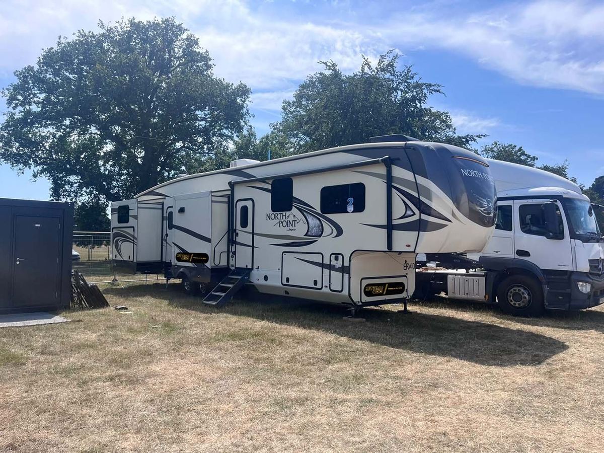 A fifth wheel arriving on site behind the truck that delivers it, sited under mature trees